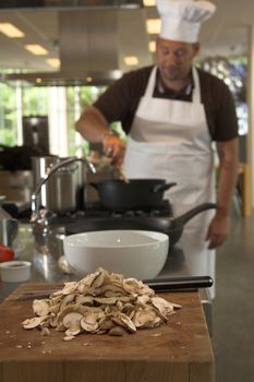 Italian chef stirring the food on the stove (focus is on the mushrooms in the front)