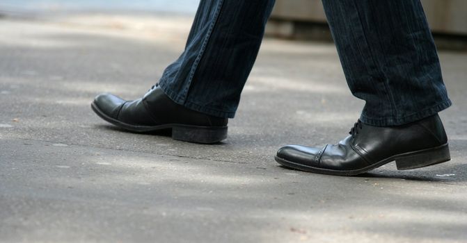 Shoes of a man walking in the street. Focus on the right shoes.