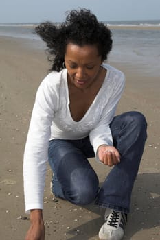 beautiful black woman looking for shells on the beach