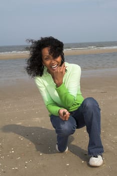 Beautiful black woman enjoying herself at the beach while searching for shells