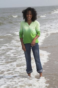 Beautiful black woman standing in the surf getting her jeans wet