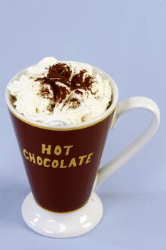A mug of hot chocolate with whipped cream over light blue background