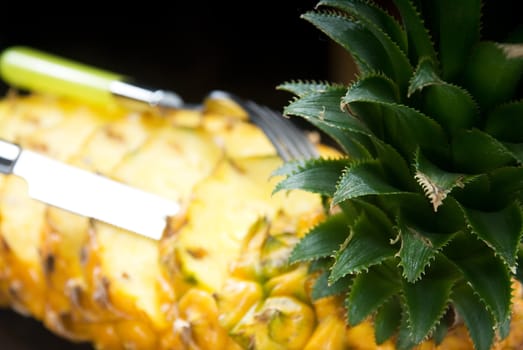 ripe vibrant pineapple sliced on a black plate with knife and fork