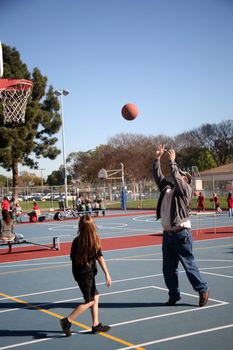 Father wearing an insulin pump and showing his daughter his technique of shooting a basketball