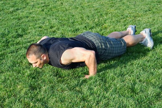 Male athlete doing push ups on the grass on a sunny afternoon.