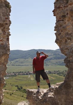 Man scrutinizing the horizon from a rocky fortress ruin in a mountainous area.