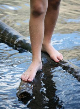 Feet of a child standing on a log in the water