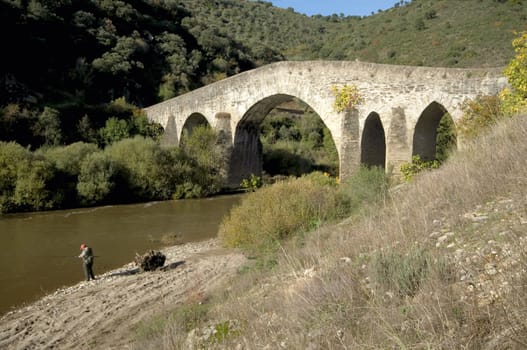 Fisherman near a medieval bridge over the Sabor river in Portugal
