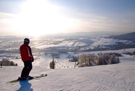Male skier standing on slope. Winter mountain landscape. Bright sunlight.