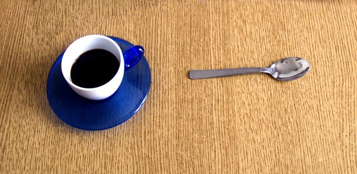 A cup of coffe and a metal spoon on wooden table