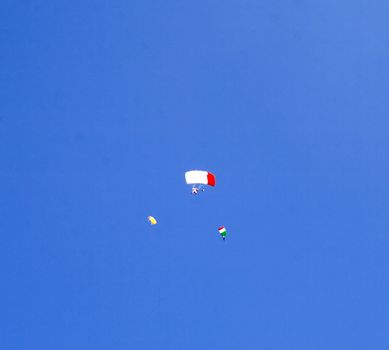 Three parachutists fly in deep blue sky