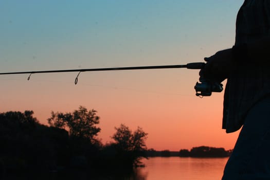 Silouette of man fishing the riverbank at dusk