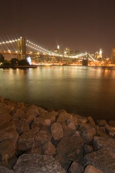 night photo of lighted brooklyn bridge in new york, rocks in foreground