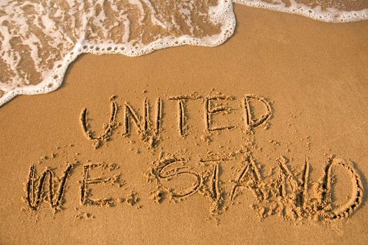 UNITED WE STAND sign written on a beach, water approaching