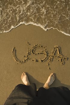 USA sign written in sand on a beach, man feet visible