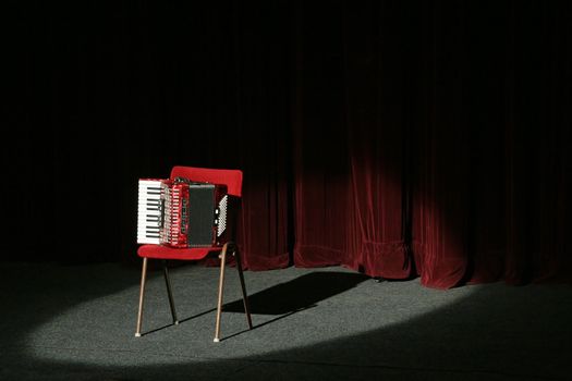 accordion on stage, lighted with a spot light, velvet curtain in background
