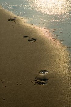 three wet footprints on a beach, small water