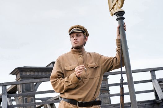 Soldier with a gun in uniform of World War I, smoking at tram stop. Costume accord the times of World War I. Photo made at cinema city Cinevilla in Latvia.