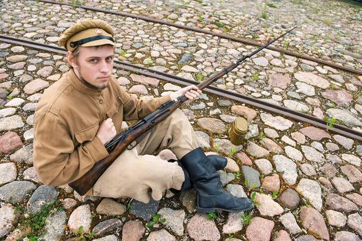 Soldier with gun and boiler in uniform of World War I, sit down and resting on the pavement. Costume accord the times of World War I. Photo made at cinema city Cinevilla in Latvia. Cockade on the hat do not contain trade mark. 