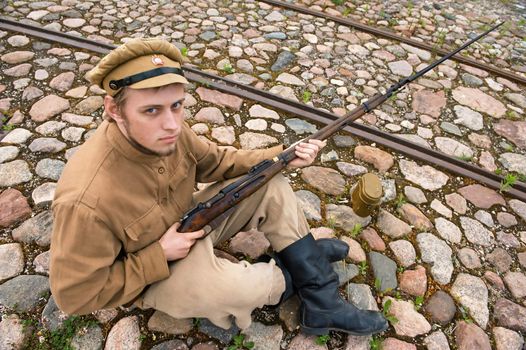 Soldier with gun and boiler in uniform of World War I, sit down and resting on the pavement. Costume accord the times of World War I. Photo made at cinema city Cinevilla in Latvia. Cockade on the hat do not contain trade mark. 