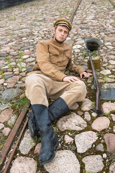 Soldier with gun and boiler in uniform of World War I, resting on the pavement. Costume accord the times of World War I. Photo made at cinema city Cinevilla in Latvia. 