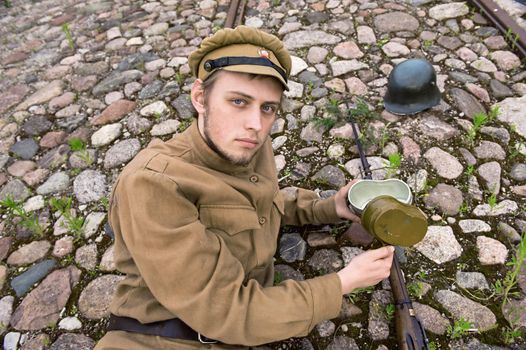 Soldier with gun and boiler in uniform of World War I, resting on the pavement. Costume accord the times of World War I. Photo made at cinema city Cinevilla in Latvia. Cockade on the hat do not contain trade mark. 