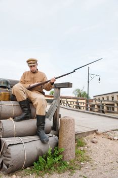 Soldier with helmet and gun sitting on the bundles. Costume accord the times of World War I. Photo made at cinema city Cinevilla in Latvia.