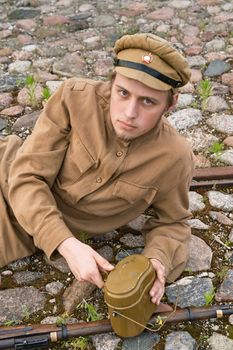 Soldier with gun and boiler in uniform of World War I, resting on the pavement. Costume accord the times of World War I. Photo made at cinema city Cinevilla in Latvia. Cockade on the hat do not contain trade mark. 