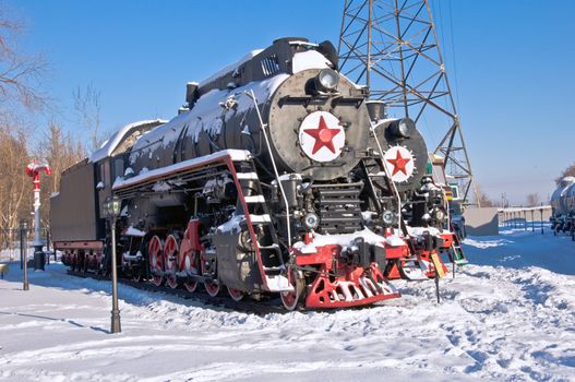 Steam locomotive beside a railway station platform. Winter. Retro train.