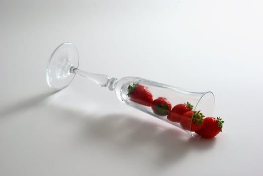 Strawberries spilled from wineglass lying on white background