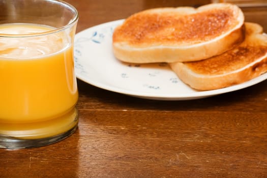 Close crop of two slices of toast and a bottle of orange juice on a worn table. focus is on the juice
