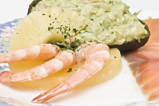 Avocado salad decorated with prawns, a slice of pineapple and a slice of salmon.