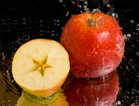 full apple and half with water splashing on black