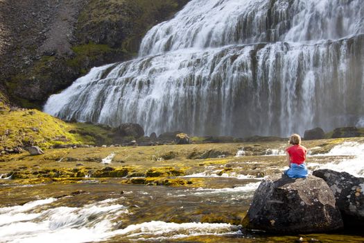 Young women relax on the rock near the Dynjandi waterfall in Iceland - westfjords.