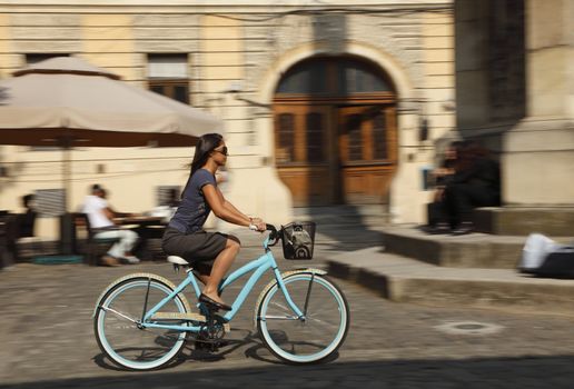 Panning image of a young woman riding her bicycle in a traditional city square.