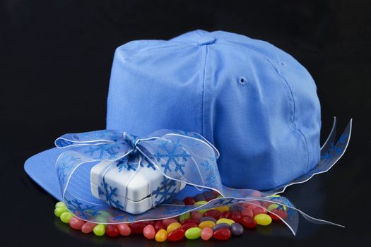 Blue baseball cap, blue ribbon around a white jewelry box placed on colorful jellybeans on black background reflect the sweet romance of love and sports