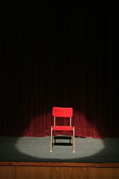 red chair on theatre stage lighted with spotlight, red curtain in background