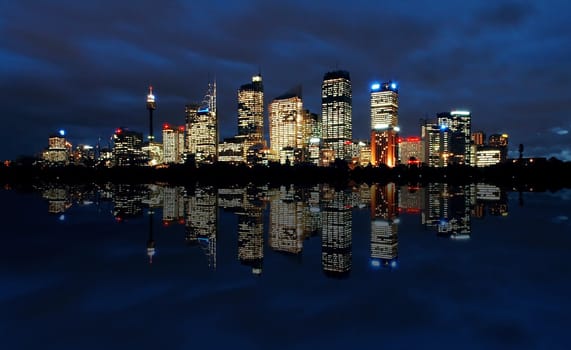 sydney cbd panorama at night, buildings reflection in water, dark cloudy night sky