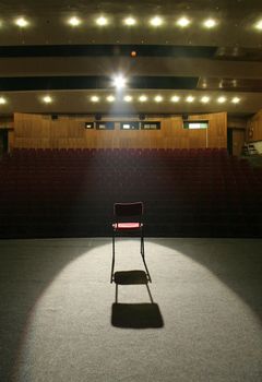 red chair on brown stage lighted with a spotlight, empty seats in background
