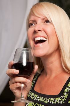 Beautiful blonde smiling woman at an evening social gathering tasting wine.