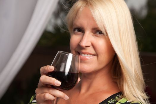 Beautiful blonde smiling woman at an evening social gathering tasting wine.