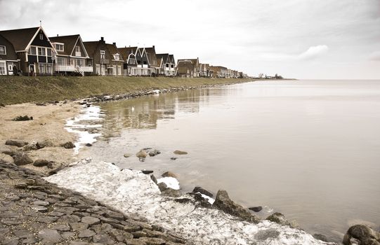 Old Dutch fishing village on dark and cloudy, rainy day in winter with snow and some melting ice at the lake. Image with old age colors. 