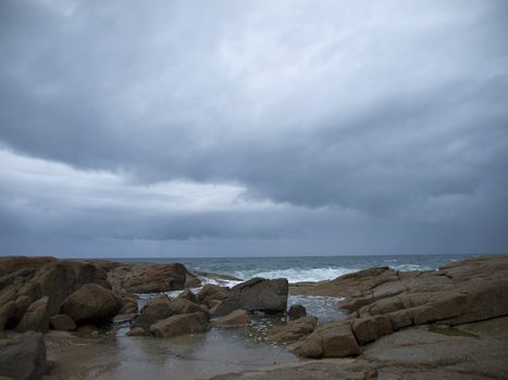 The storm threatens the rocky beach. The storm has already begun on the background.