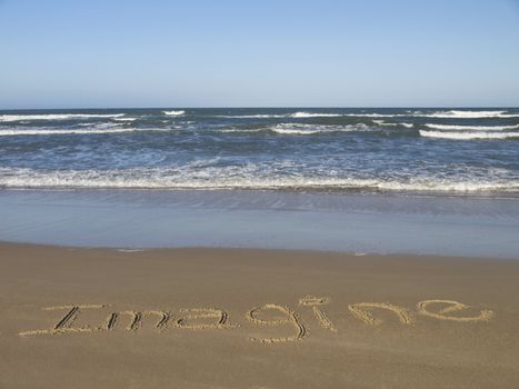 IMAGINE written on the sand beside the ocean.