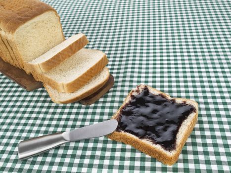 A slice of bread spread with jam beside the loaf of bread.