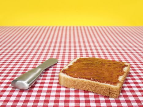 A slice of bread spread with jam and a knife over the table.