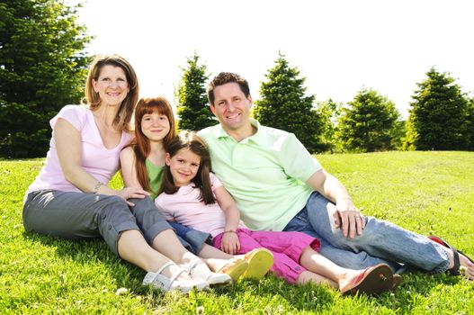 Portrait of happy family of four sitting on grass at the park hugging