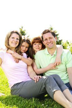 Portrait of happy family of four sitting on grass at the park hugging