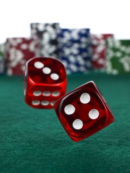 Two red dices rolling over a green felt. Out of focus stack of colorful chips on the background.