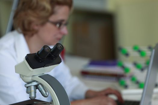 Image of a researcher working on her workplace in a laboratory.Selective focus on the microscope.
